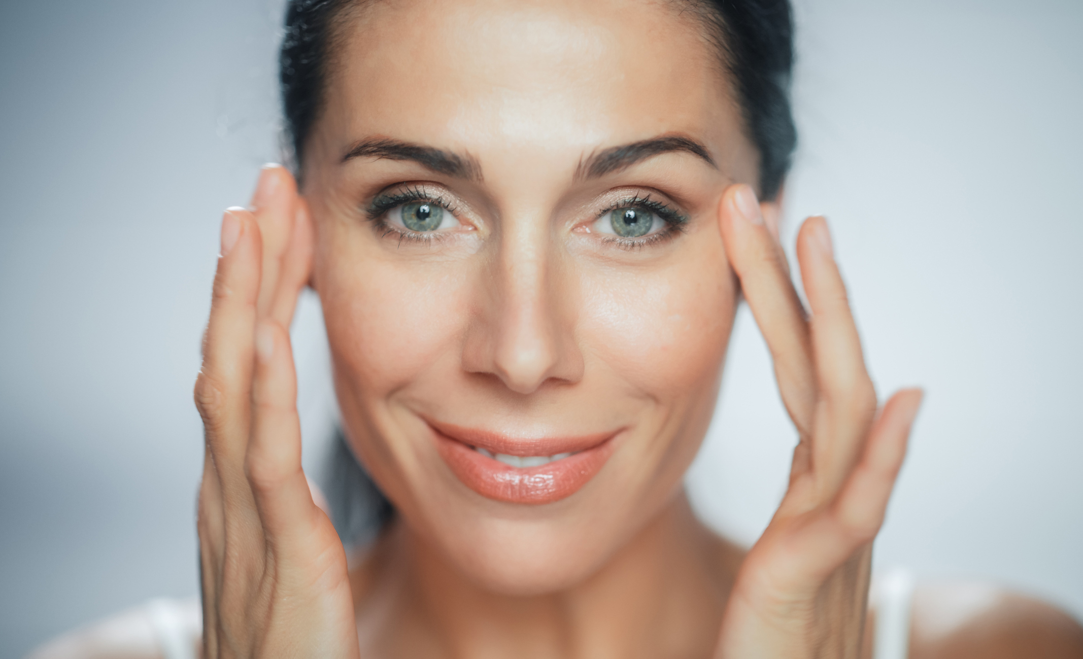 Beautiful Caucasian Woman Touches Her Perfect Face with Soft Skin, Smiling. Female Enjoying Her Beauty, High Self Esteem, Wellness. Natural Cosmetic Skincare Products. Portrait on Isolated Background Microdermabrasion in Akron, OH